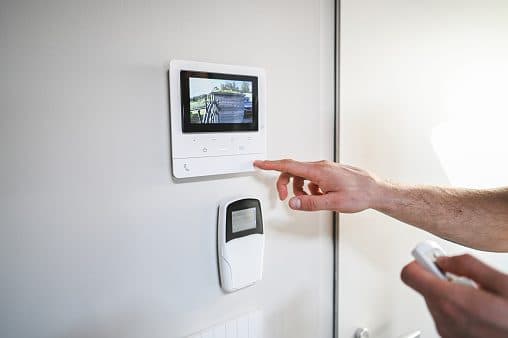Hand pointing at a white security control panel on the wall