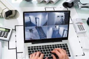 Laptop displaying security camera feeds on a desk next to architectural blueprint layouts