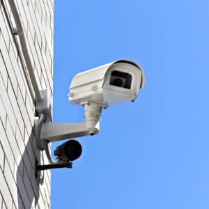 Outdoor security camera mounted on brick wall under clear blue sky