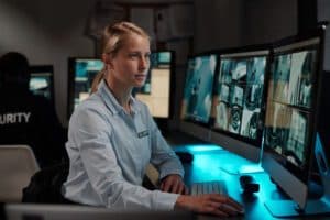 A professional female security dispatcher monitoring multi-screen security feeds in a control room