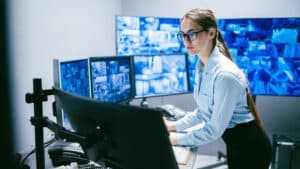 A security professional in a control room in front of circular arrays of security display feeds checking telemetry