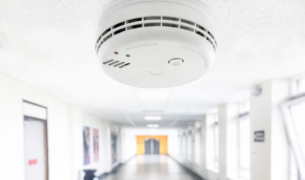 A white smoke detector ceiling mounted in a long hallway