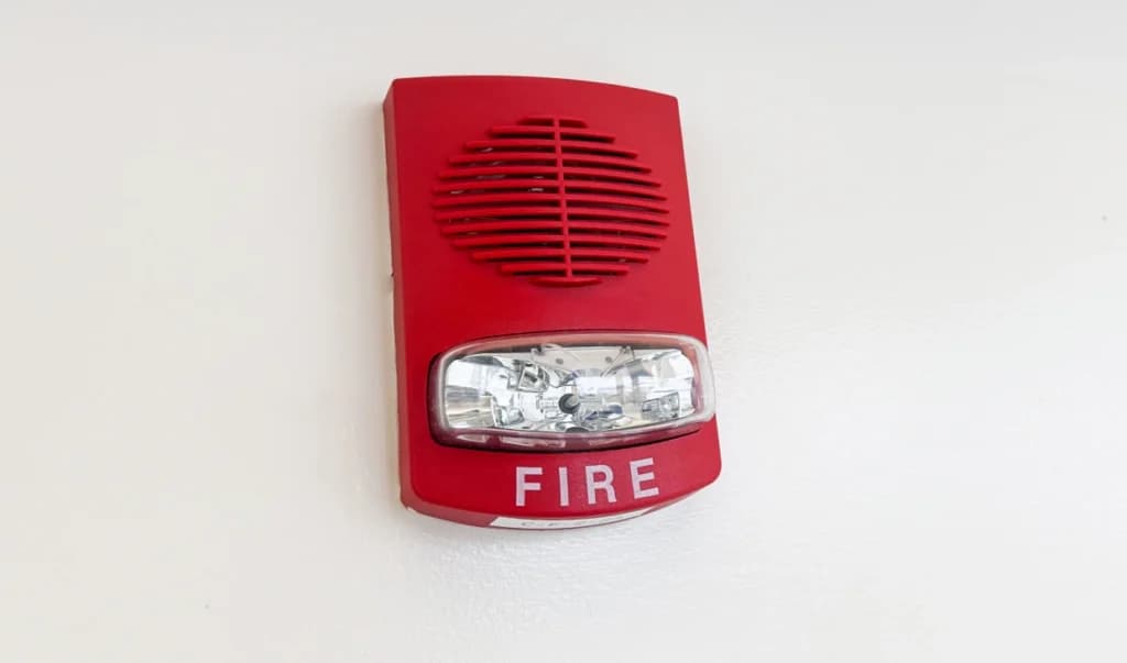 A red fire alarm pull station and strobe mounted on a white wall