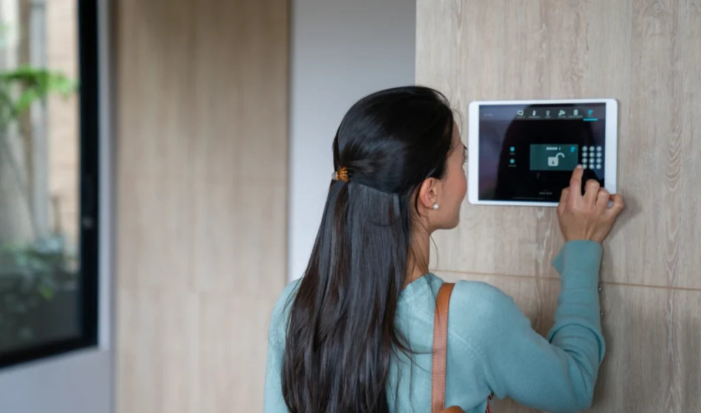 A woman using a home security control panel tablet mounted on a wall