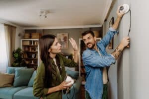 A happy young couple mounting and adjusting a smart home security camera on a living room wall