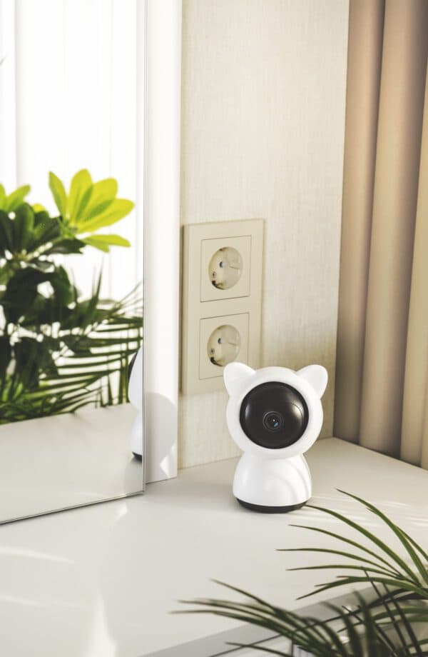 A cute white cat-eared smart camera sitting on a white table counter next to a mirror