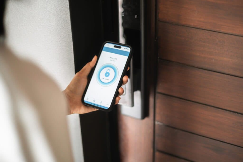 A person holding a smartphone showing the smart lock interface in front of a modern smart door lock