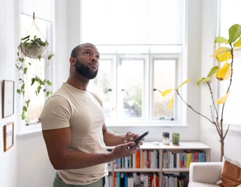 A man in a bright living room using a smartphone to manage smart home functions