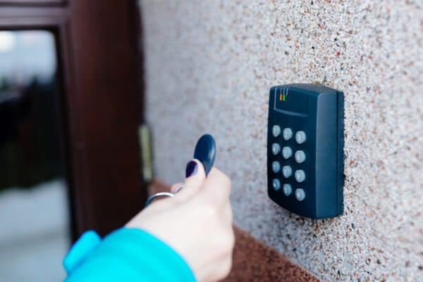 Hand using key fob on wall mounted scanner next to glass door