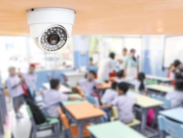 Indoor security camera mounted on classroom ceiling with students sitting at desks