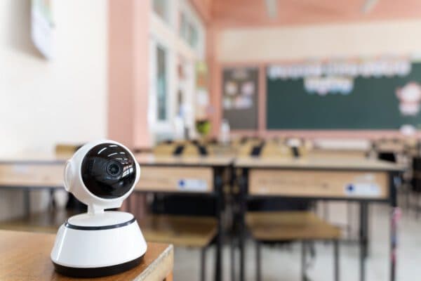 Small camera standing on desk in a school classroom looking towards rows of desks