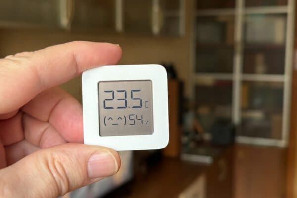 Holding a small white digital temperature display screen showing 23.5 degrees Celsius