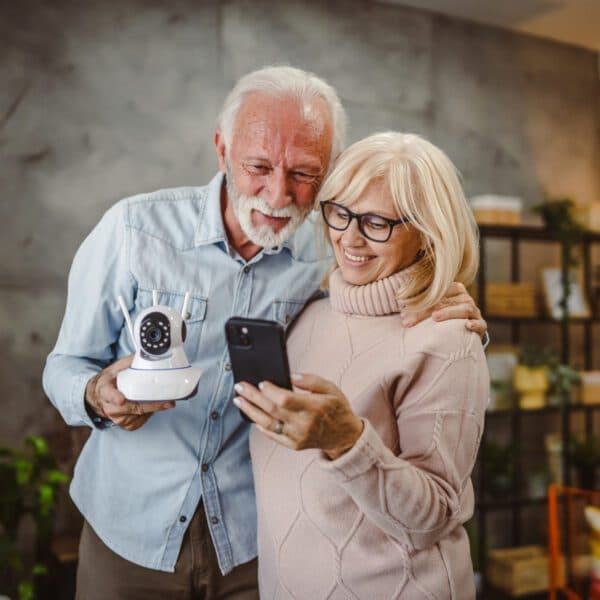 Happy older couple holding a smart phone and a security camera
